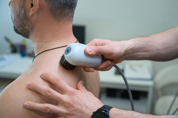 Physiotherapist treating patient for upper back pain with ultrasonic device  Stock Photo by svitlanah