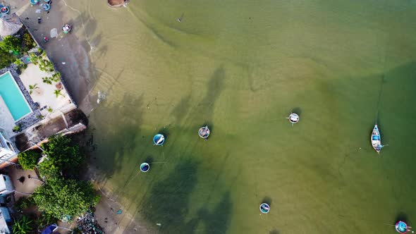 Aerial bottom up view over small beach in green water with round boats. Slow motion alt