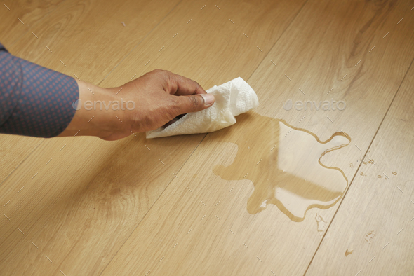 hand wiping spilled tea with paper napkin on floor ,