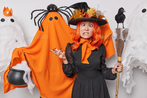 People and October holiday concept. Funny woman makes grimace wears wizard hat and dress poses with