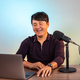 Smiling asian man looking at the laptop in a studio with microphone - PhotoDune Item for Sale
