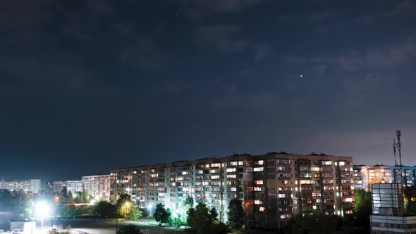 Stars and Night Clouds Move Over Multi-story Buildings. Night City. Timelapse alt
