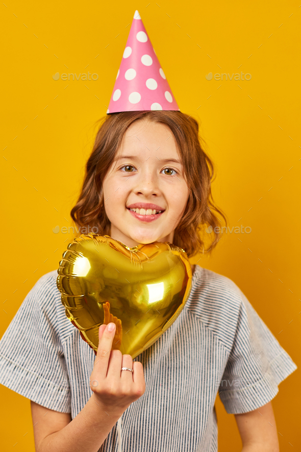 Cheerful, positive ten years birthday girl in party hat