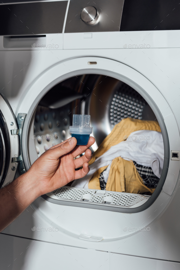cropped view of man holding measuring cup with blue detergent near washing  machine with dirty Stock Photo by LightFieldStudios
