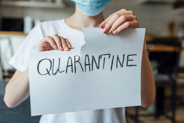 Cropped view of woman in medical mask tearing card with quarantine lettering