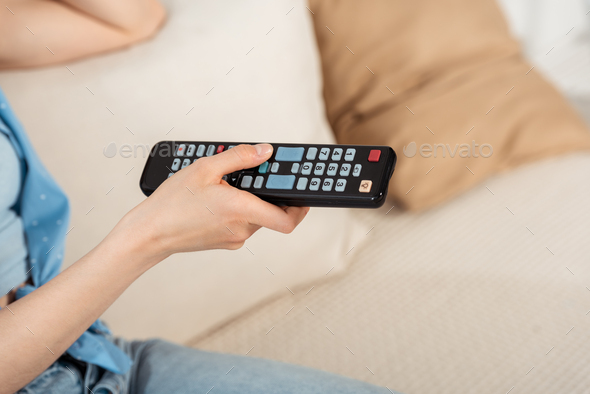 Cropped view of girl holding remote controller on couch