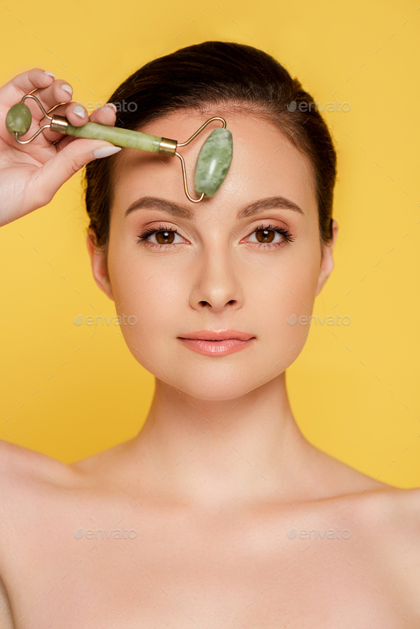 Beautiful Naked Woman Using Jade Roller On Face Isolated On Yellow