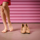 Female legs puts on high-heeled shoes wrapped in rustic beige craft paper on pink background.  - PhotoDune Item for Sale