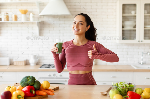 Fitness diet concept. Sporty woman drinking a green detox smoothie for  breakfast in the kitchen. Stock Photo