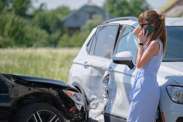 Stressed driver talking on sellphone on roadside near her smashed vehicle