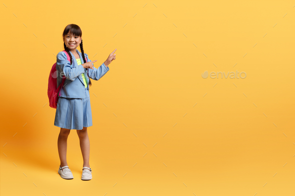 Cute korean school girl in uniform pointing at copy space