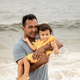Father holding toddler daughter in his arms at the beach and enjoying fresh breeze - PhotoDune Item for Sale