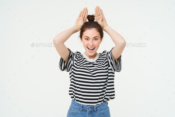 Enthusiastic young woman, holding hands on top of head, animal ears gesture, laughing and smiling