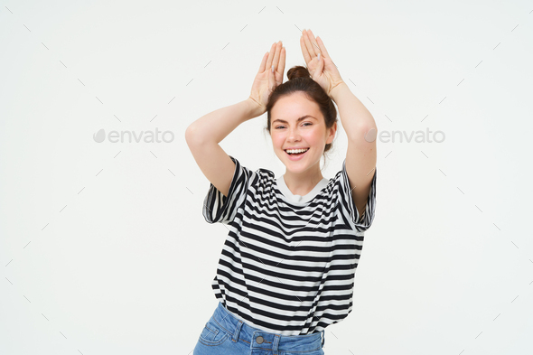 Young woman laughing, showing animal floppy ears gesture with hands on top of head, smiling and