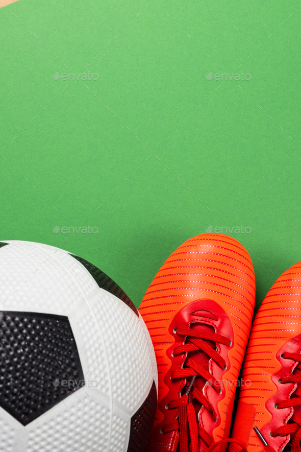 Image of orange football boots and football on green background with copy space