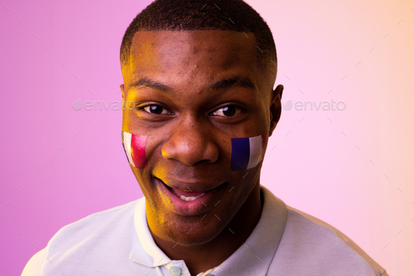 Portrait of happy african american male supporter with flag of france over pink lighting