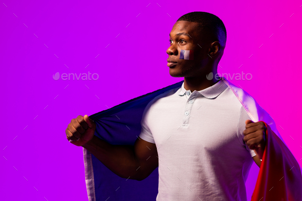 Happy african american male supporter with flag of france over pink lighting