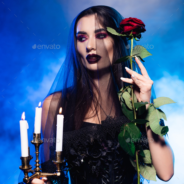 mysterious young woman with black makeup in veil looking away near rose on  blue Stock Photo by LightFieldStudios