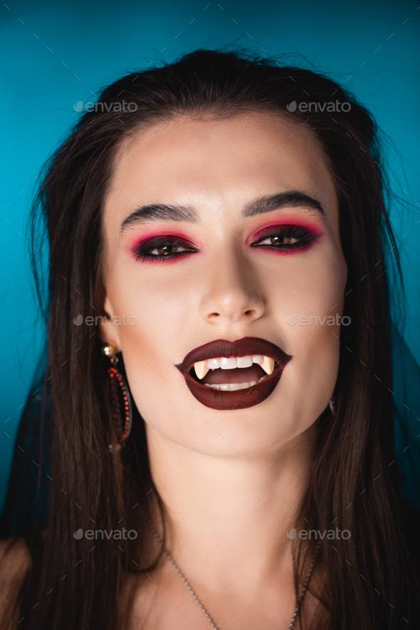 brunette vampire with black makeup and white scary teeth on blue
