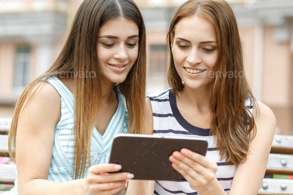 Smiling girls using tablet for online shopping outdoors