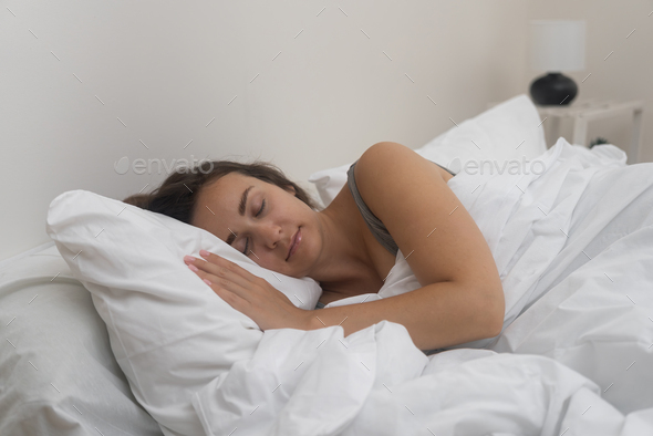 Serenely asleep, young lady rests under a white blanket comfortable orthopedic mattress in bedroom
