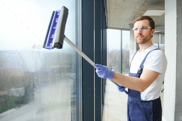 Male professional cleaning service worker in overalls cleans the windows and shop windows of a store