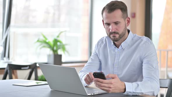 Young Man Using Laptop and Smartphone in Office  alt