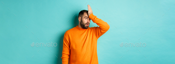 Annoyed man roll eyes and making facepalm, standing over turquoise background