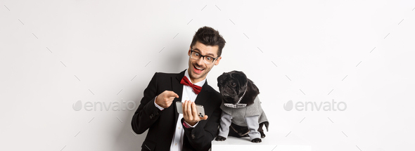 Happy dog owner showing something to pet on mobile phone, man and pug wearing fancy costumes