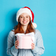 Winter holidays and Christmas Eve concept. Smiling redhead girl in sweater and Santa hat, holding - PhotoDune Item for Sale