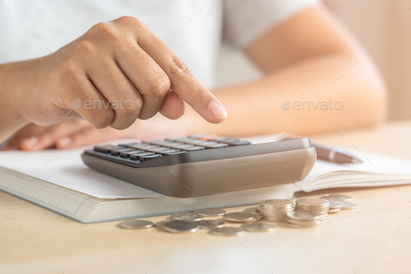 Woman using calculator doing home accounting with coins and notebook
