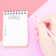 Female hand writes in a paper notebook goals close-up on pink background. - PhotoDune Item for Sale
