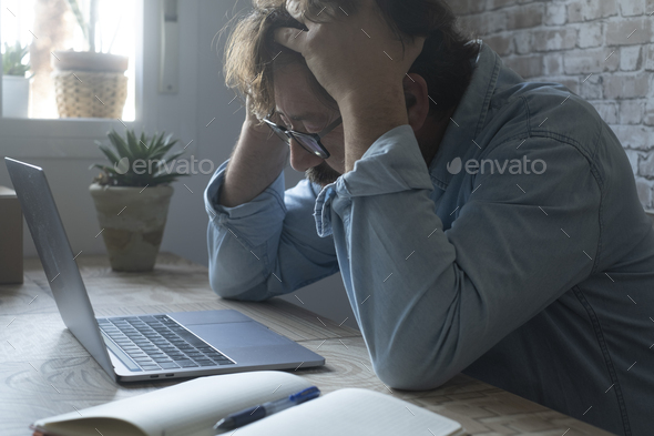 Worried and desperate stressed worker an at the desk holding his head with exhausted expression