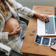An unrecognizable pregnant woman sits at a table, works on a laptop and plans for childbirth. - PhotoDune Item for Sale