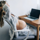 A pregnant woman takes a break from work at her laptop, sitting in a chair. - PhotoDune Item for Sale