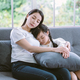 Sweet moment Asian mother is hugging to her asleep cute daughter while sitting on sofa at home. - PhotoDune Item for Sale