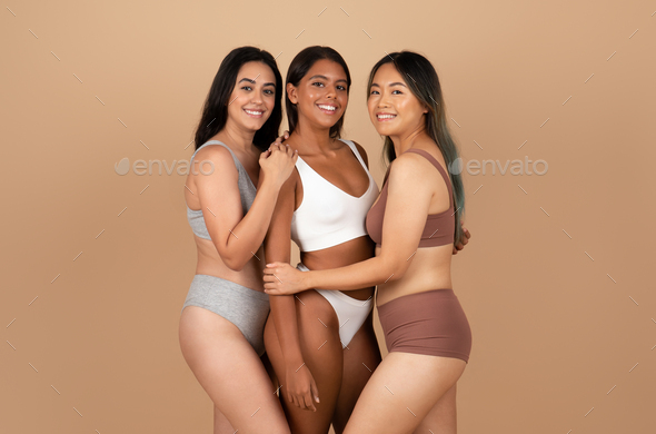 Positive young international women friends in different underwear, posing  isolated on beige Stock Photo by Prostock-studio