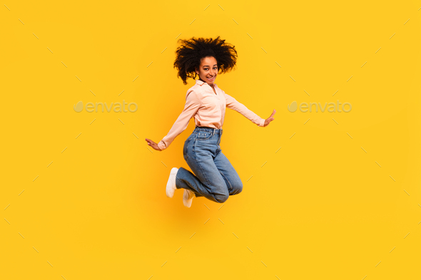 Excited black lady jumping in air and smiling at camera, female student having fun over yellow