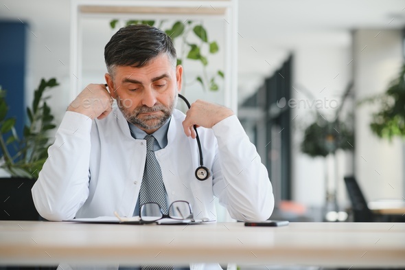 Mature doctor man at the clinic tired rubbing nose and eyes feeling fatigue and headache