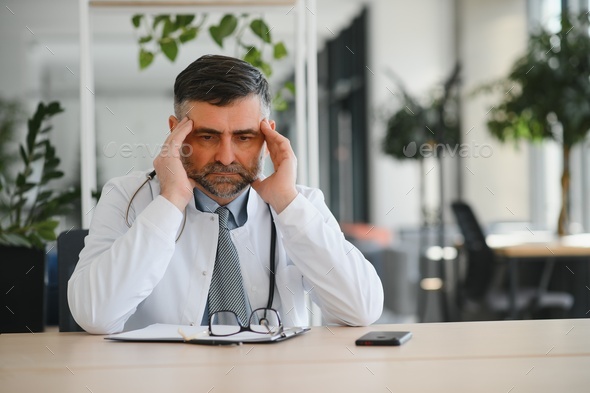 Mature doctor man at the clinic tired rubbing nose and eyes feeling fatigue and headache