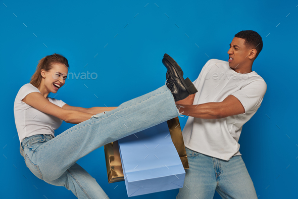 consumerism, interracial customers fighting, pulling shopping bags on blue backdrop, holiday sales
