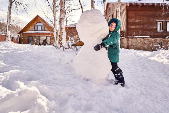 A family builds a snowman out of white snow in the yard in winter. - Stock Photo - Images