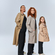 joyful redhead family in coats posing with hands in pockets on grey background, female generations - PhotoDune Item for Sale