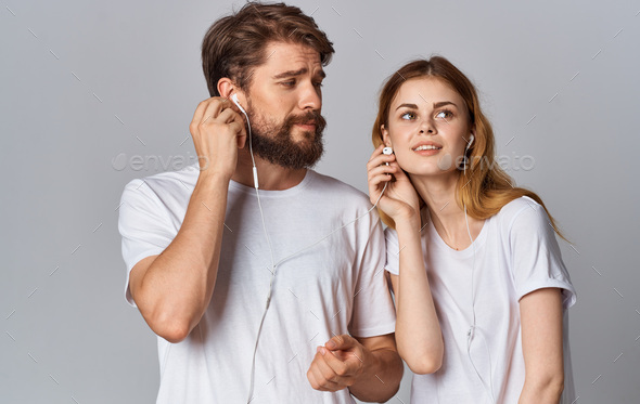 a man and a woman in white headphones stand side by side on a gray background in the same T-shirts