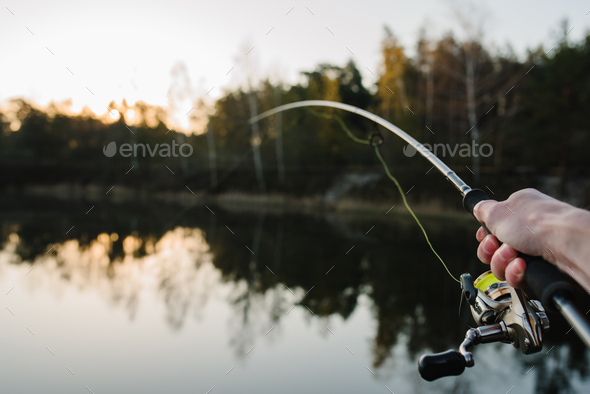 Fisherman with rod, spinning reel on the river bank. Sunrise