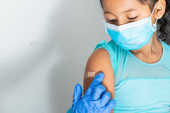 Doctor in protective gloves putting an adhesive bandage on a girl\'s arm after injecting vaccine