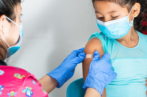 Doctor in rubber protective gloves putting an adhesive bandage on a girl\'s arm, injecting vaccine