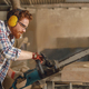 Professional carpenter in glasses is cutting wood with chainsaw on carpentry workshop - PhotoDune Item for Sale