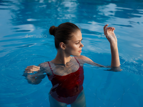 Happy woman swimming in pool in red swimsuit with loose long hair