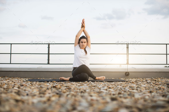 Adult meditating in pose with twisted legs on gravel roof